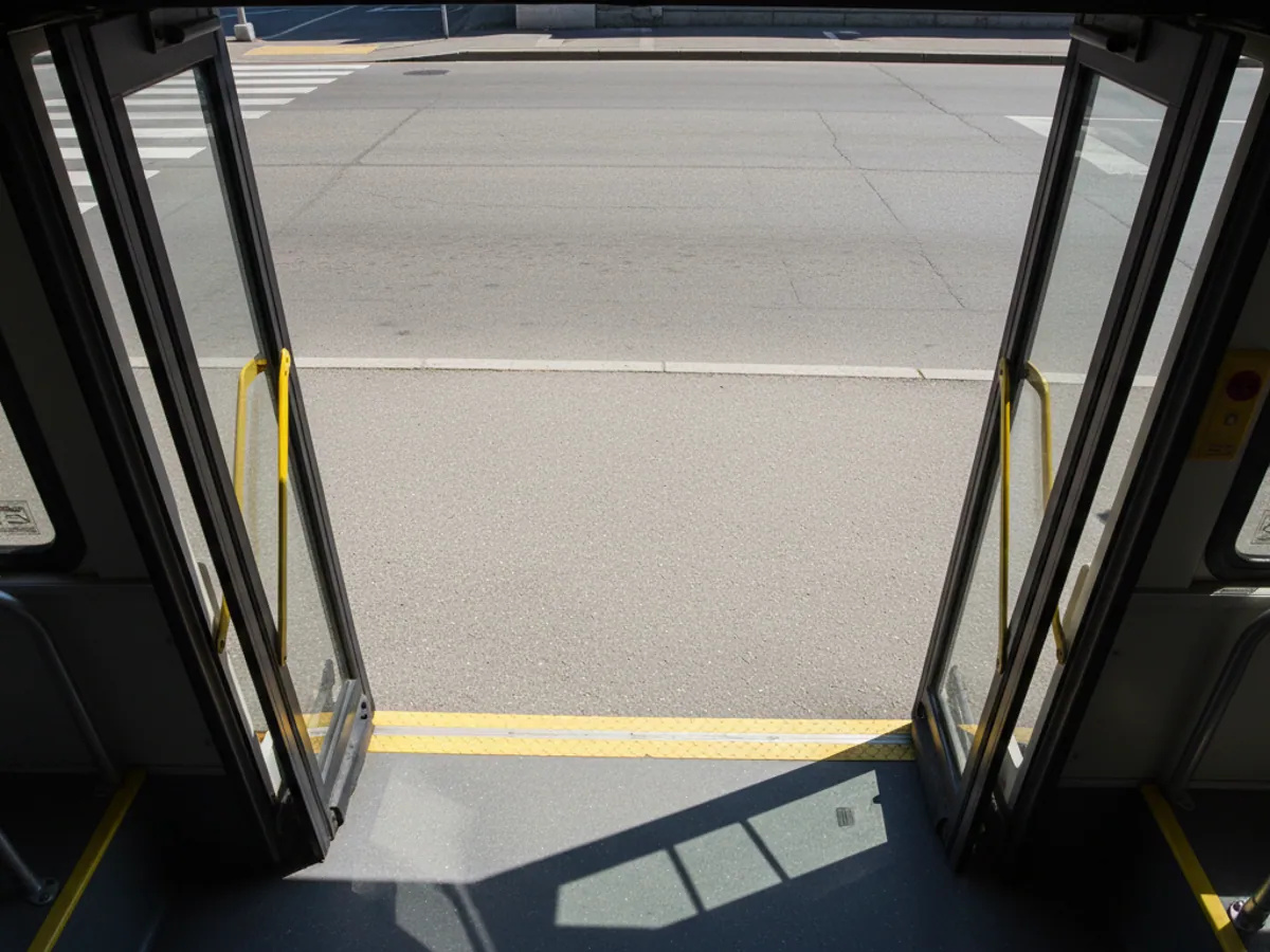 A view down from the ceiling of a bus onto the steps of an open door and the pavement