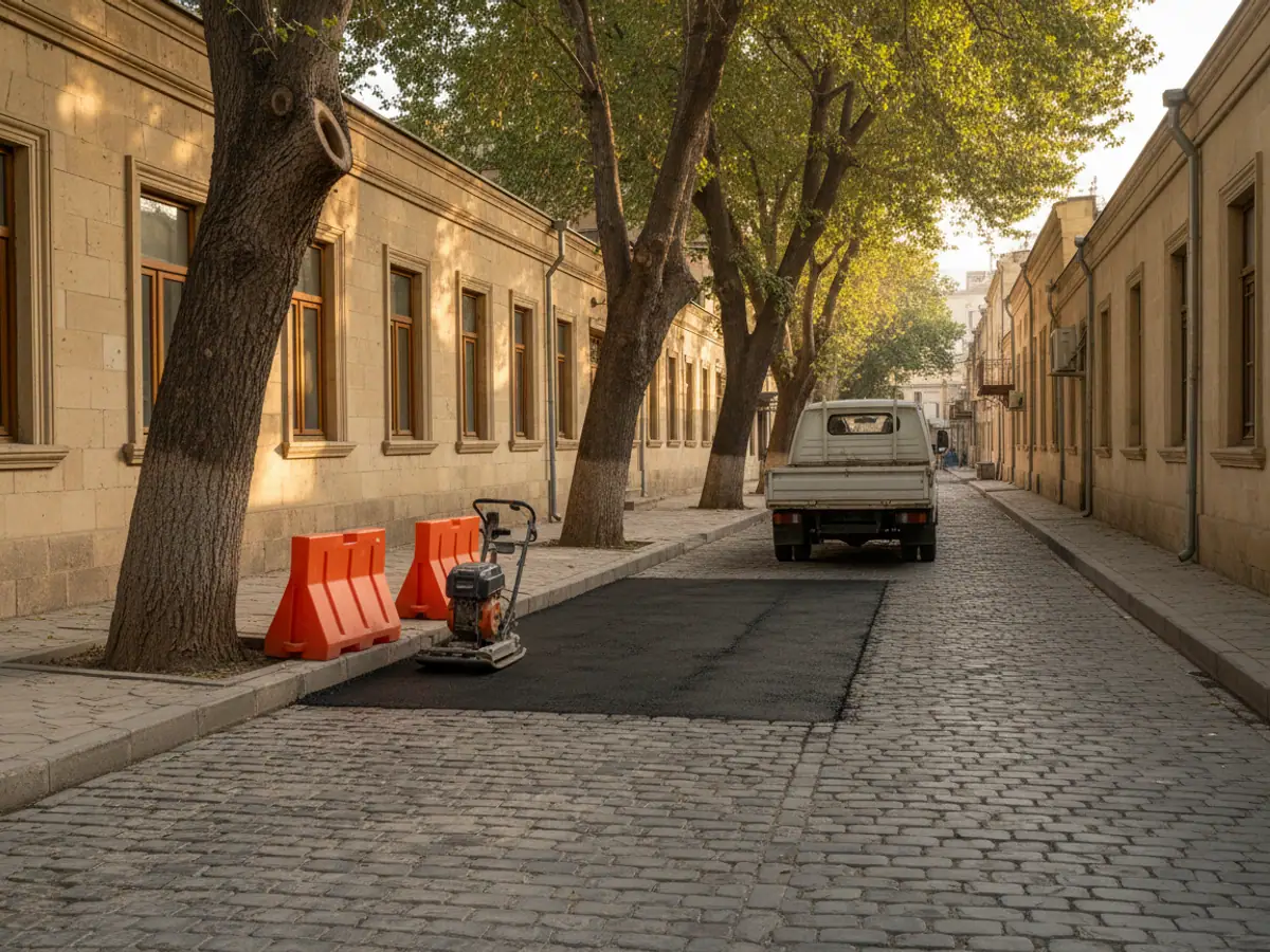 A fresh asphalt patch over a backfilled trench, with a plate compactor and a works lorry beside it