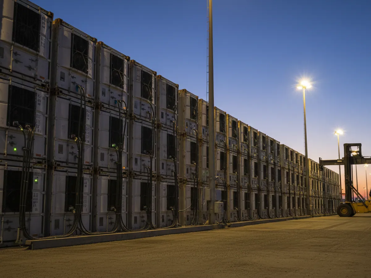 A row of reefer containers plugged into power at a terminal at dusk, indicator lights glowing