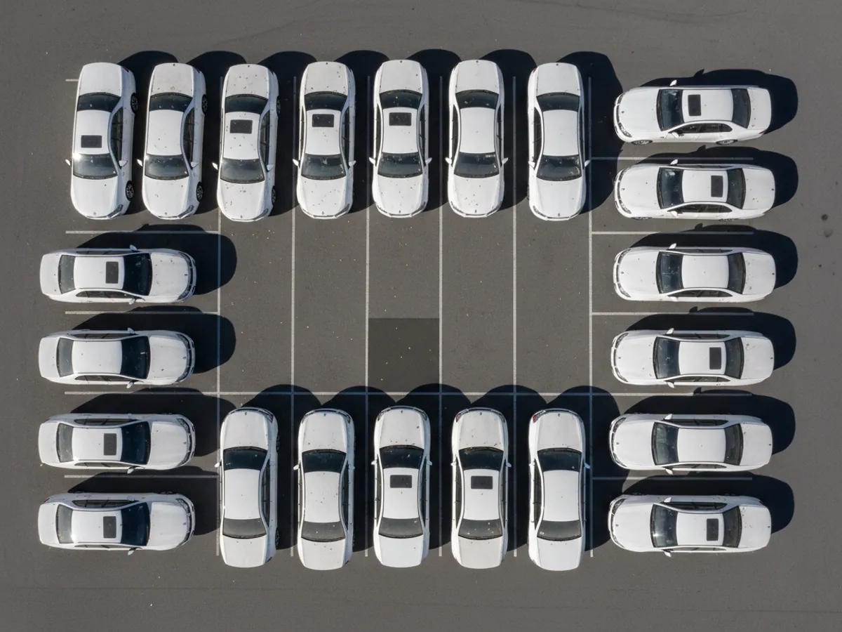 An overhead view of a car park of official saloons with dust and leaves on their roofs