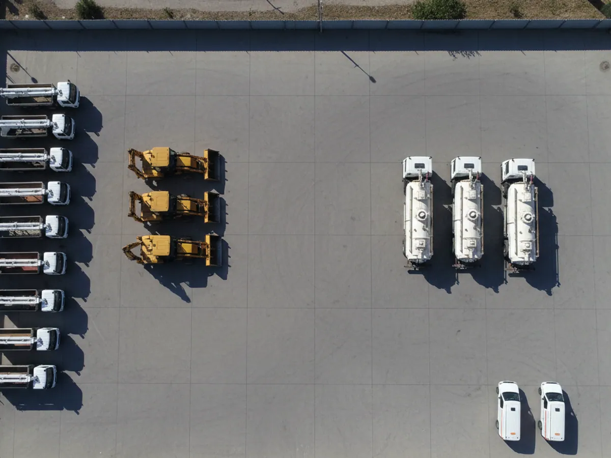 Seen from above: aerial platforms, excavators, vacuum tankers and vans parked in groups in a depot yard
